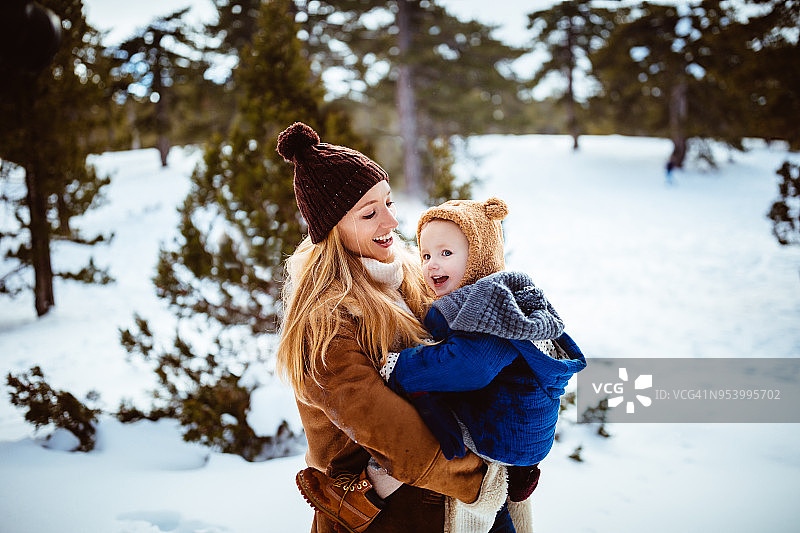 年轻的母亲在白雪覆盖的森林里拥抱小女儿图片素材