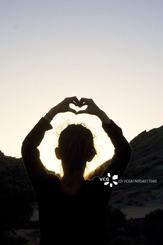 女孩在日落时用手做出心形轮廓图片素材