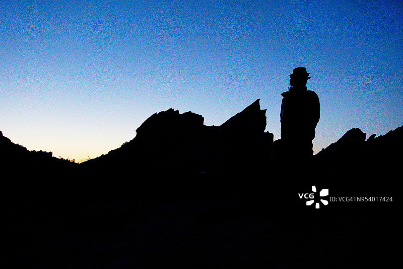 戴软呢帽的男人在日落时分于瓦斯奎兹岩石前呈现剪影图片素材