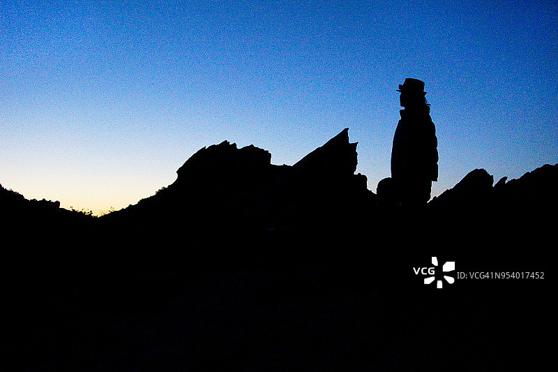 戴软呢帽的男人在日落时分于瓦斯奎兹岩石前呈现剪影图片素材