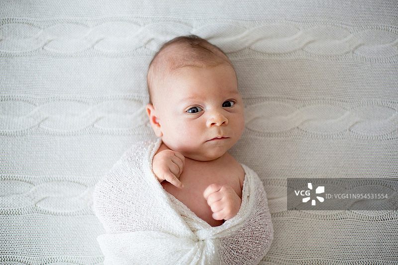 裹着白色襁褓好奇地看着镜头的新生男婴图片素材