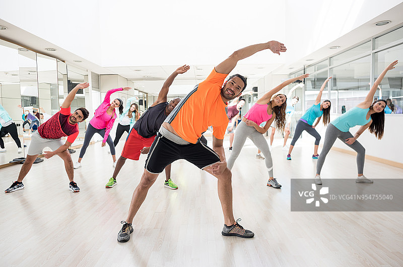 快乐的指导员指导他的班级在健身房伸展运动图片素材