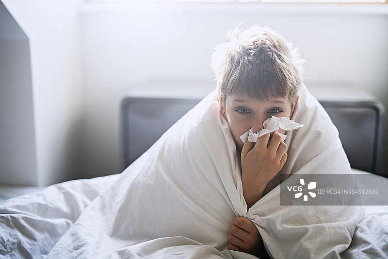 生病的小男孩躺在床上擤鼻涕图片素材