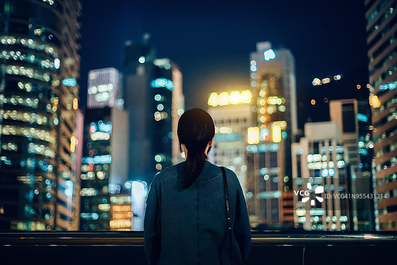 女子站在屋顶露台上，眺望壮观的城市夜景图片素材