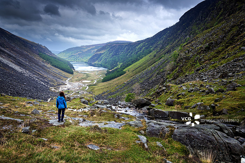 在爱尔兰威克洛山脉的格伦达洛山谷，沿着格伦尼洛山谷步道向外看的女人，一个暴风雨的春天下午图片素材