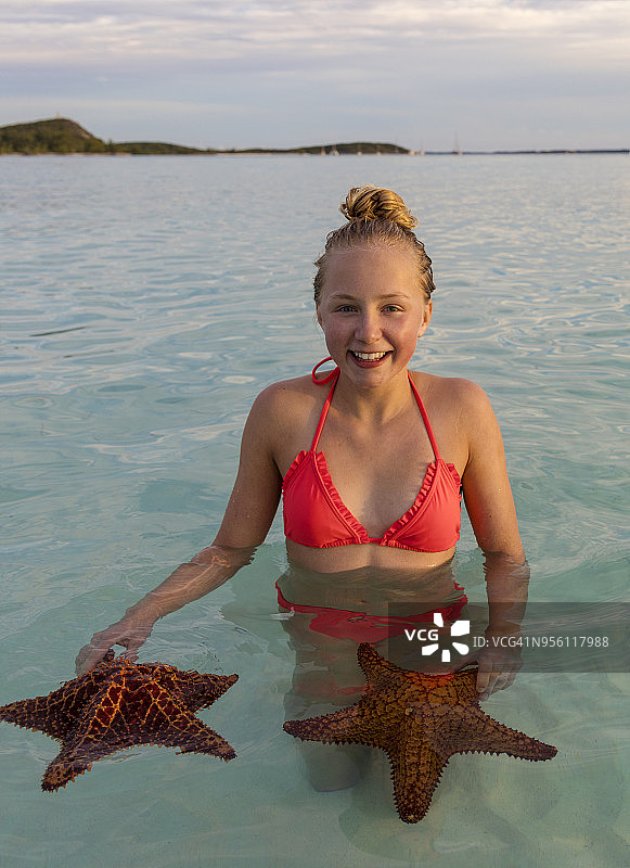 女孩在海洋中手持海星微笑，地点：斯托金岛，埃克苏马斯群岛，巴哈马图片素材