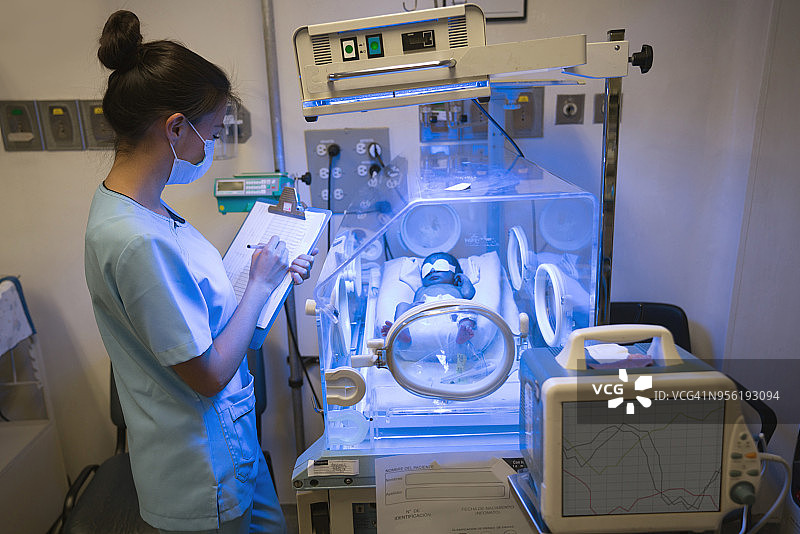 新生儿重症监护室的护士检查在保温箱中接受黄疸治疗的新生儿患者图片素材