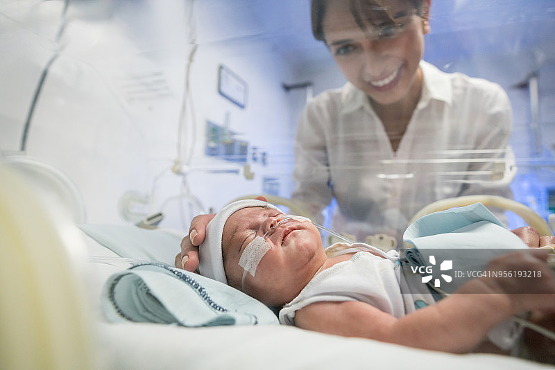 年轻漂亮的妈妈在育婴箱里爱抚着她的早产新生儿图片素材