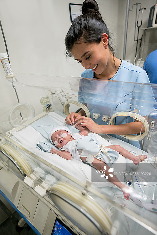美丽的护士在保育箱中照顾早产新生儿图片素材