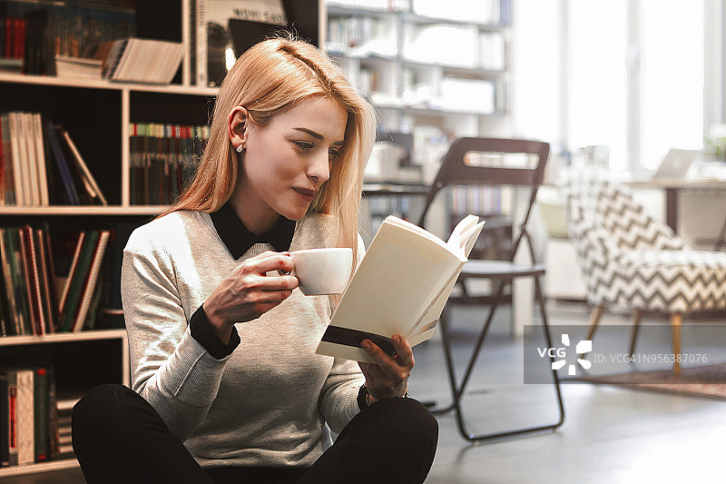 在图书馆享受咖啡和书籍的年轻女人图片素材