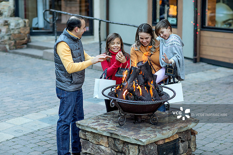 在豪华山区滑雪胜地小镇，一家人提着购物袋在壁炉旁取暖图片素材