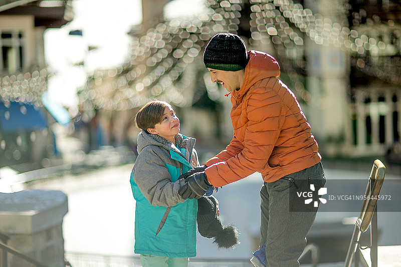 阳光明媚的日子里，西班牙裔父亲在滑雪胜地为女儿戴上手套图片素材