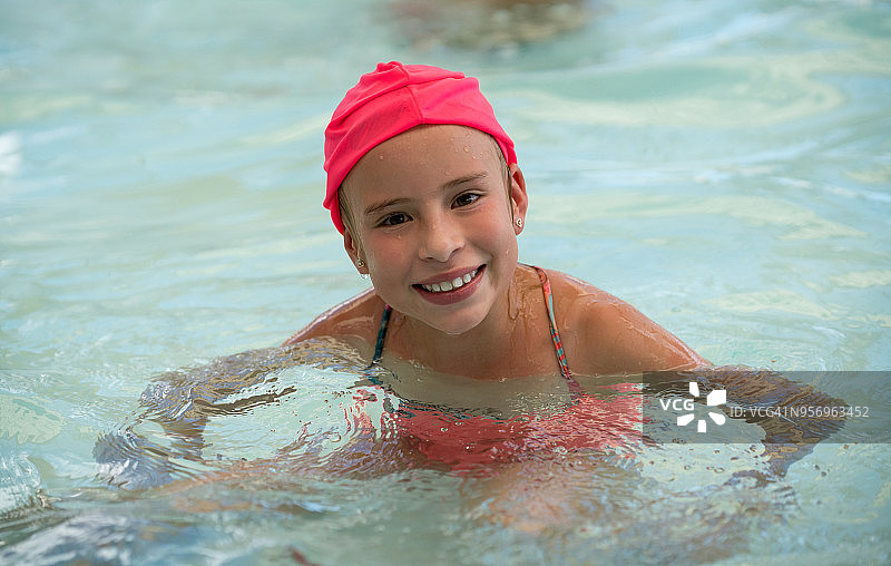 在游泳池里玩得很开心，对着镜头微笑的可爱小女孩图片素材