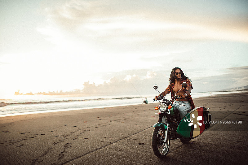 年轻的冲浪者骑着摩托车在海滩上图片素材