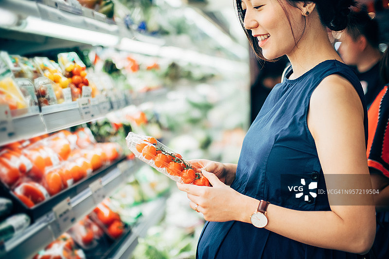 微笑的亚洲孕妇在超市购买新鲜有机蔬菜图片素材