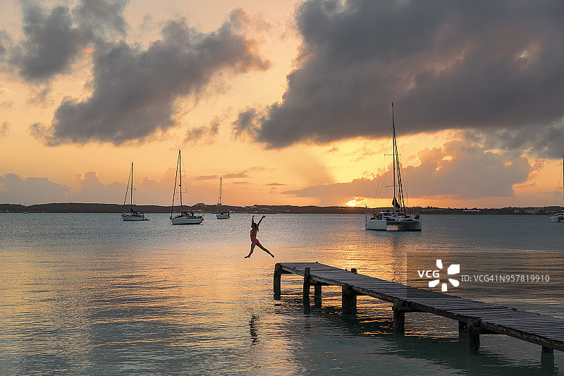 日落时分，女孩从码头上跳下_斯托金岛_埃克苏马斯群岛_巴哈马图片素材
