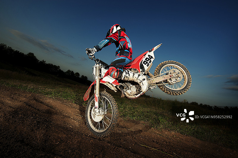 男子在黄昏时于田野上用越野摩托车表演特技图片素材