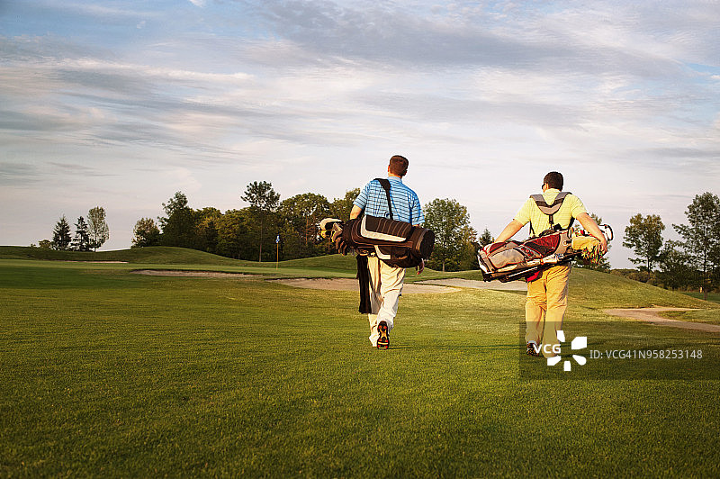 男性高尔夫球手在日落时分背着球包走在球场上的背影图片素材
