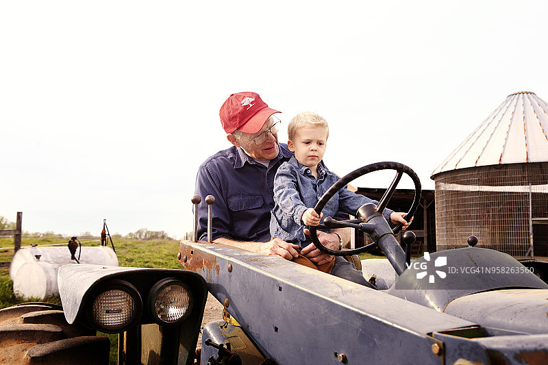 祖父和男孩驾驶拖拉机在晴朗天空下的低角度景观图片素材