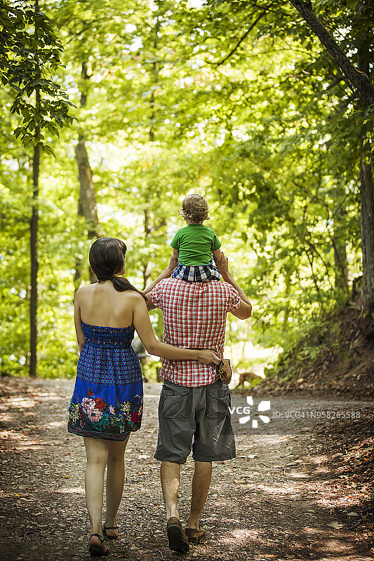 男人背着儿子和妻子在森林里散步的背影图片素材