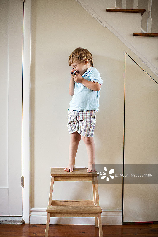 快乐的男孩站在家里的凳子上图片素材