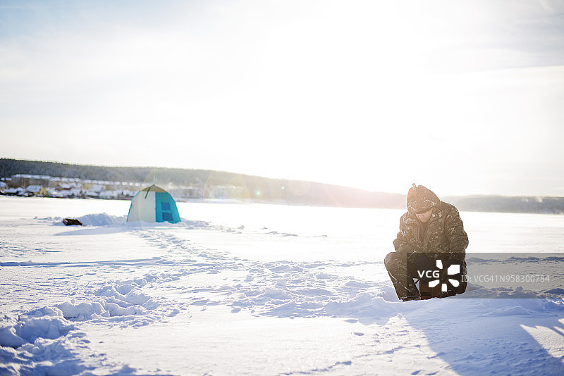 男人在阳光明媚的日子里坐在结冰的湖面上，以天空为背景图片素材