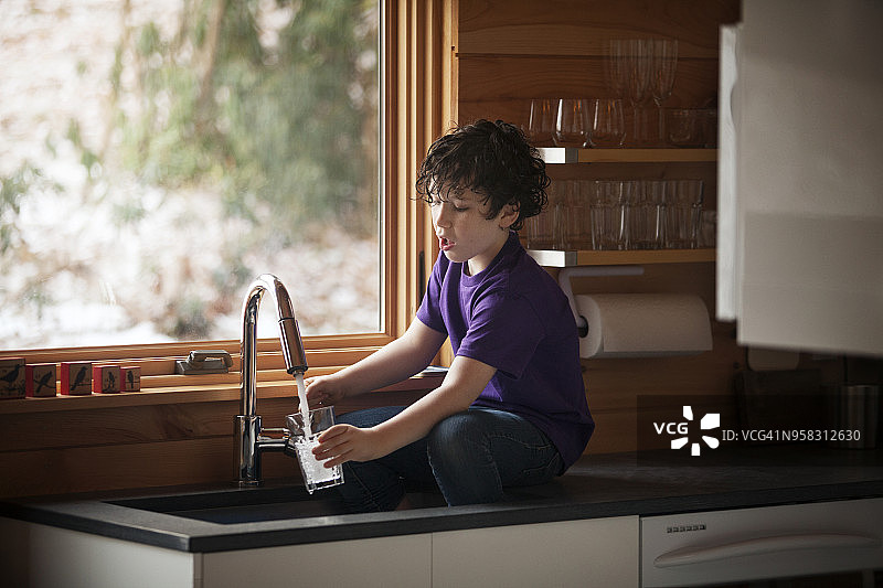 男孩坐在厨房柜台旁倒水图片素材