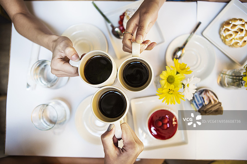 朋友们在餐厅餐桌旁用咖啡杯碰杯的特写图片素材