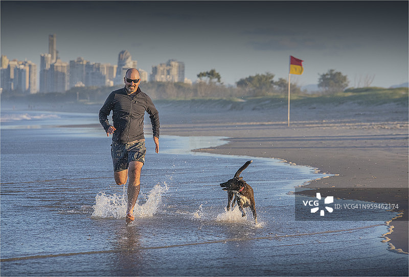 在昆士兰州黄金海岸沙嘴与他的狗在海滩上奔跑的男人图片素材