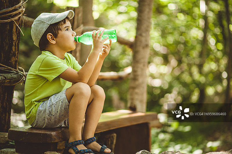 男孩坐在树林的长椅上喝水图片素材