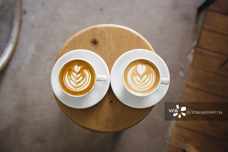 俯拍圆形木桌上的两个拉花咖啡杯图片素材