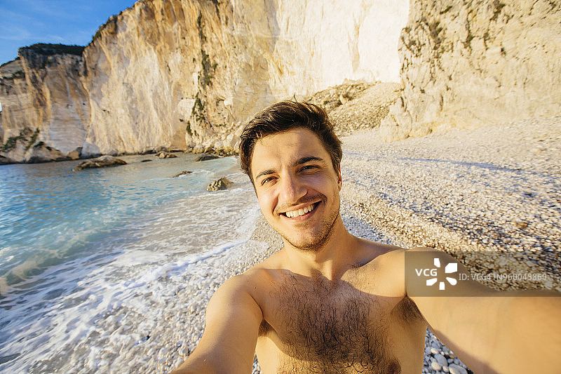 快乐的年轻男子在希腊海滩上自拍图片素材