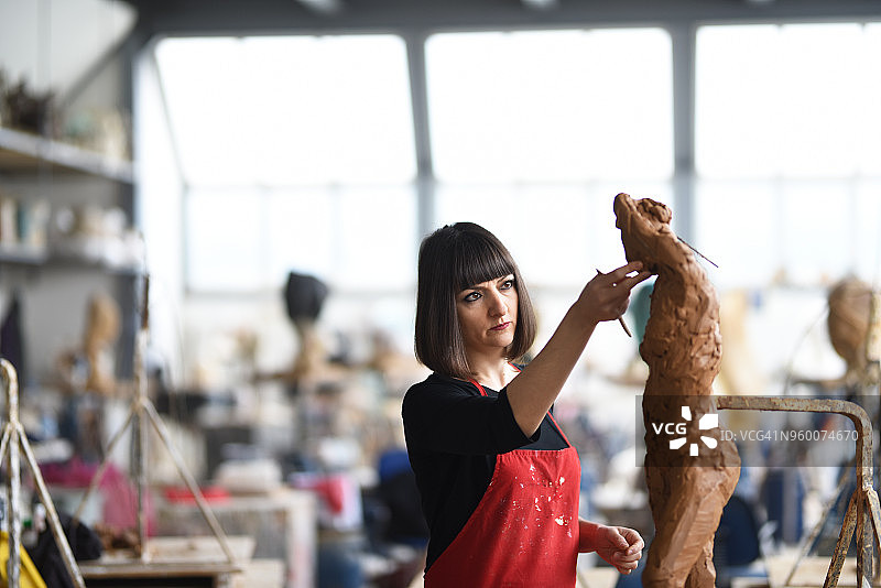年轻女雕塑家在工作室工作图片素材
