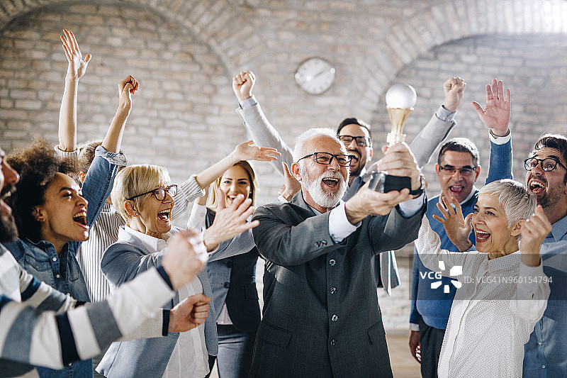一大群快乐的商务人士在办公室里举着奖杯图片素材