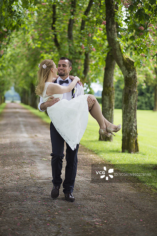 新郎抱着新娘穿过绿树成荫的小路图片素材