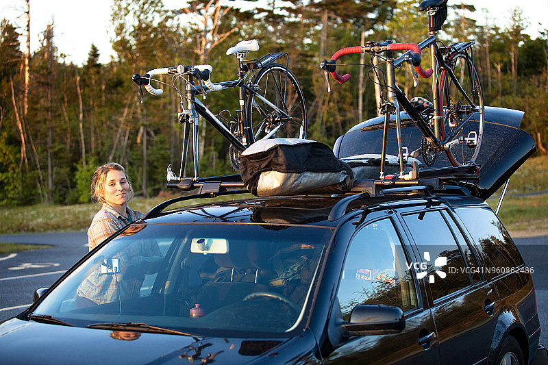 站在街边停放的、车顶有山地自行车的汽车旁的微笑女人图片素材