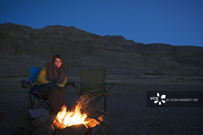 坐在篝火旁的女人肖像，背景是山脉和蓝天（阿尔沃德沙漠）图片素材