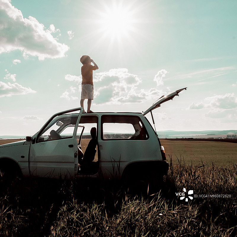 晴朗的一天，无忧无虑的男孩站在田野上汽车车顶的仰视角度照片图片素材