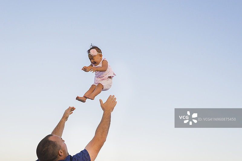 父亲将女儿抛向空中，以晴朗的天空为背景的低角度视图图片素材