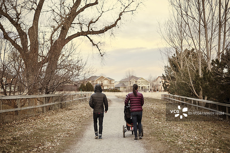 冬季，男人和女人推着婴儿车在路上行走的背影图片素材