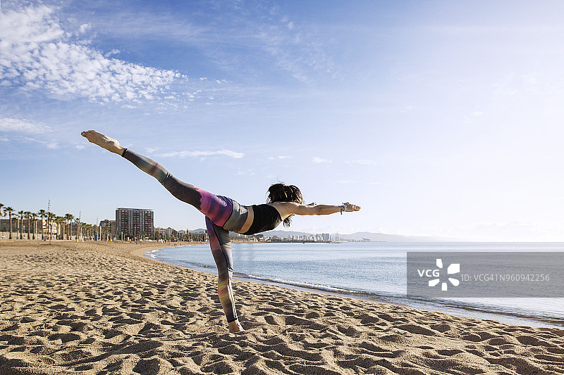决心在海滩上以战士三式姿势练习瑜伽的女人图片素材