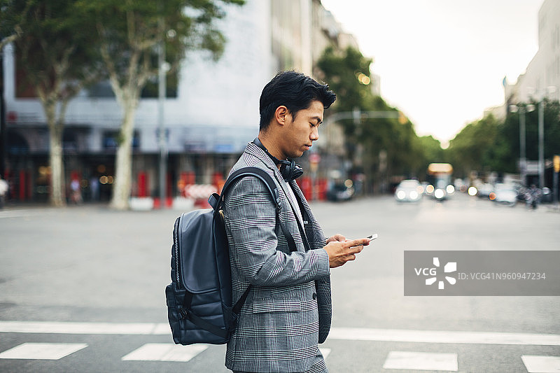 商务人士背着背包站在街上使用智能手机的侧视图图片素材