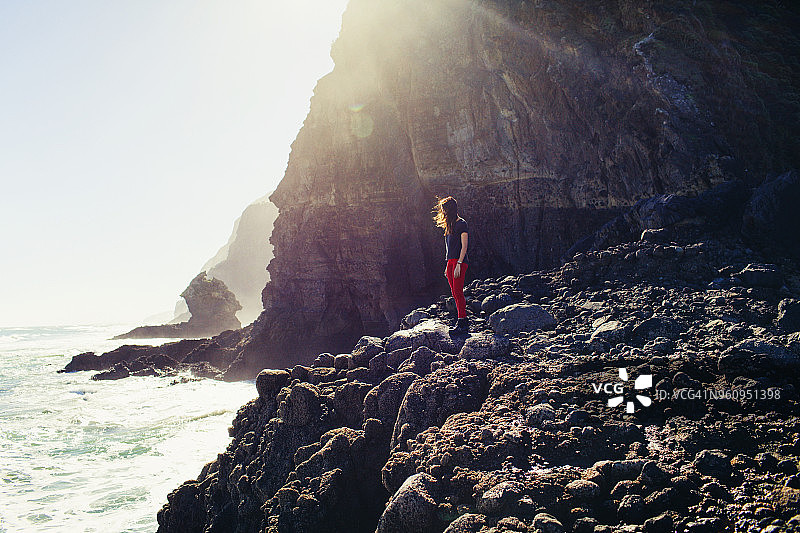 侧视图：在阳光明媚的日子里站在岩石岸边的女人图片素材