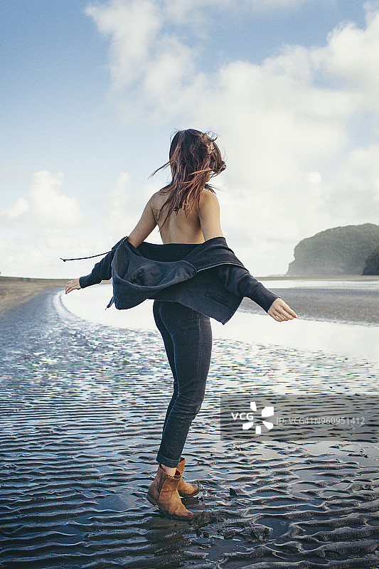 在多云天空下站在潮湿海滩上的女子侧影图片素材