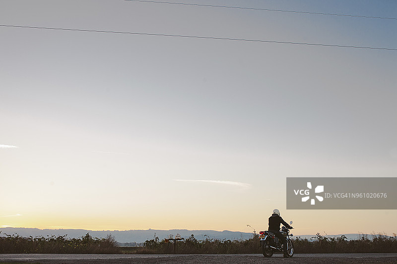日落时，坐在自行车上的男骑车人以天空为背景的背影图片素材