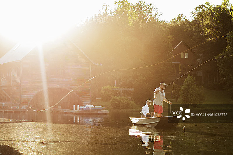 阳光明媚的日子里，男人和朋友在划艇中在湖里抛钓鱼线图片素材