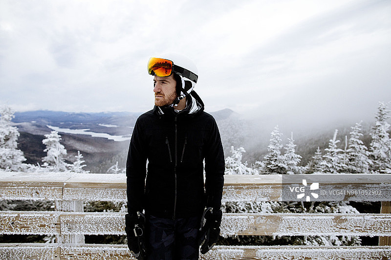 雾天里站在冰冻木栅栏旁、穿着滑雪服沉思的男人图片素材