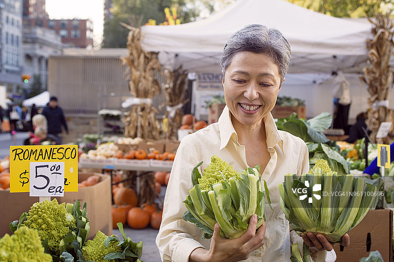 快乐的中年妇女在农贸市场检查宝塔花菜图片素材