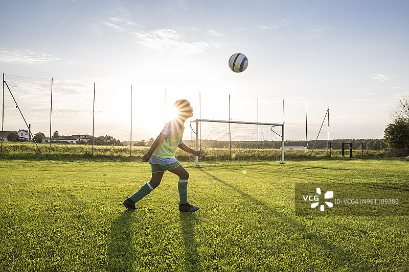 夕阳下在足球场上头球的年轻足球运动员图片素材