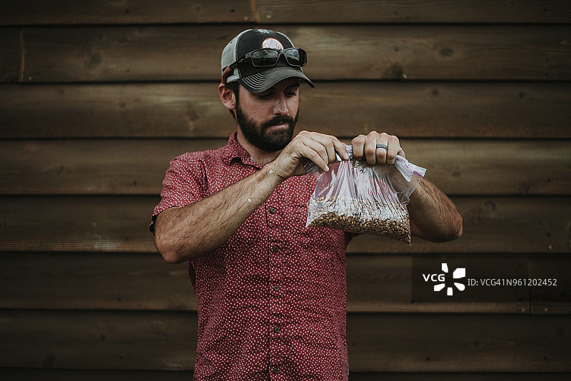 男人靠在木墙边，手里拿着一袋花生图片素材